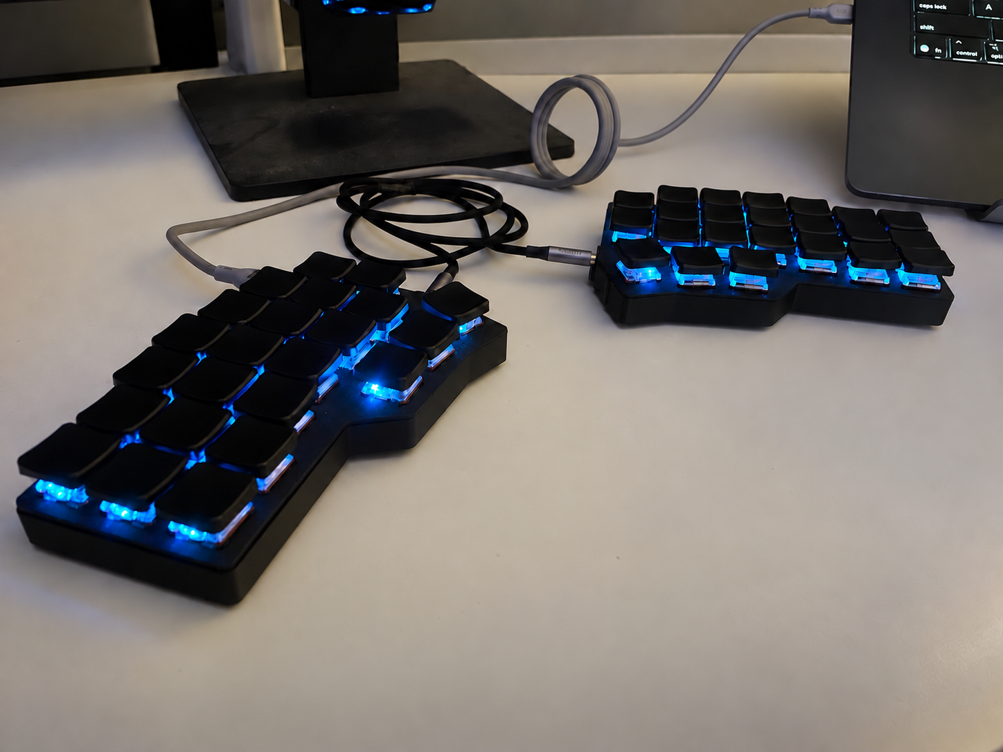 The finished Corne split keyboard on my desk, with black enclosures and keycaps lit by blue LEDs
