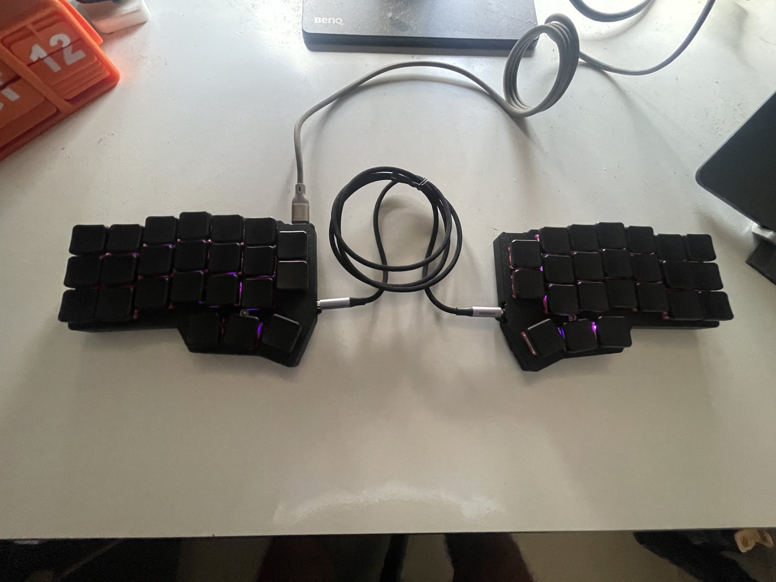 The finished Corne split keyboard with black keycaps and black printed enclosures, connected by a cable